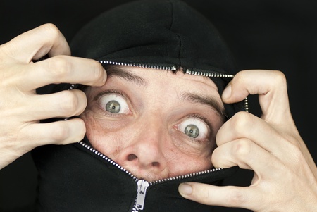 Close-up of a shocked man with the hood of his sweatshirt zipped up to his nose trying to break free.の写真素材