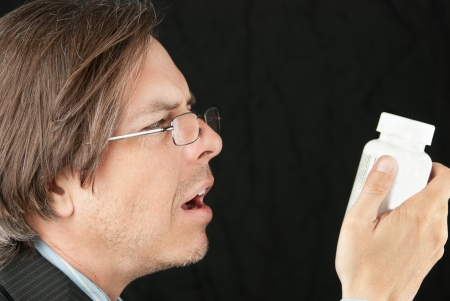 Close-up of a casual businessman wearing glasses trying to read a pill bottle label.の写真素材