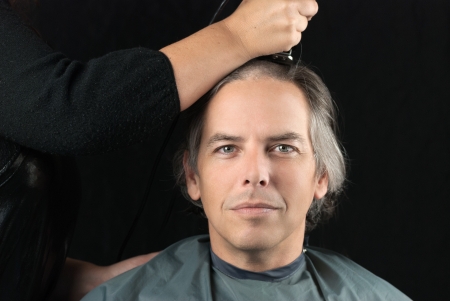 Close-up of a serious man looking to camera while his long hair is shaved off for a cancer fundraiser.の写真素材