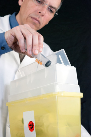 Close-up of a Doctor dropping a syringe with butterfly needle attached into sharps container の写真素材