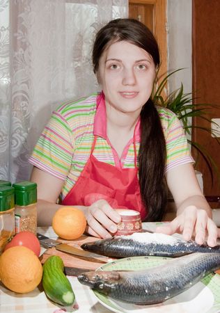 Young woman is corning a herring fish  in kitchenの写真素材