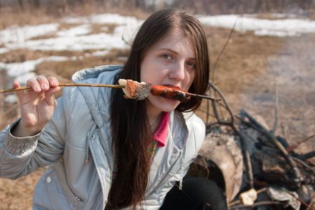 Girl eating sausage cooking by bonfire in  natureの写真素材