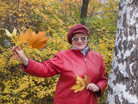 Smiling old lady in red stays in autumn park. の写真素材