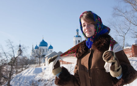 girl in russian traditional kerchief against Orthodox monastery in  Bogolubovo.