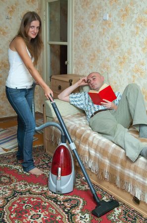 yang womam doing housecleaning and man resting over sofaの写真素材