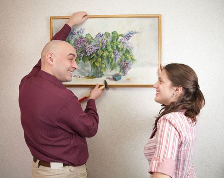 A young and attractive couple hanging up an art picture on their wallの写真素材
