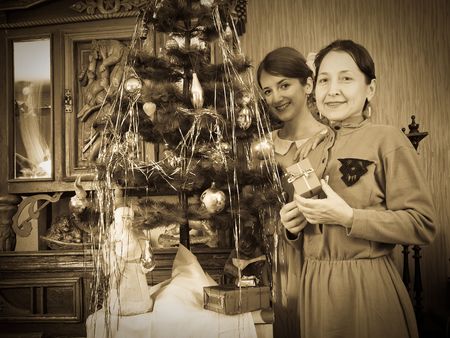 Retro photo of  daughter with mother near Christmas tree at homeの写真素材