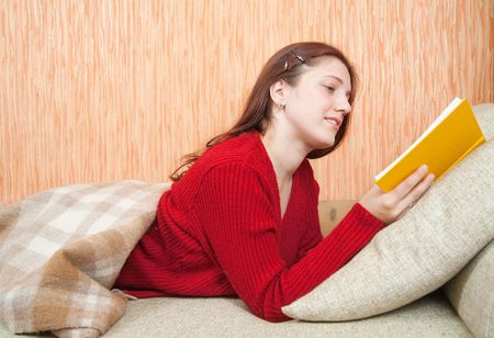 Relaxed woman lying on sofa in livingroom enjoying reading book の写真素材