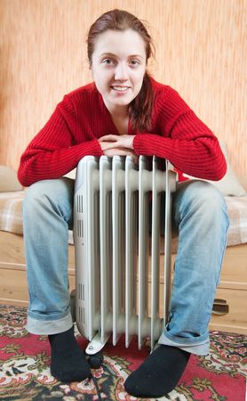 young smiling girl is sitting by a oil heater の写真素材
