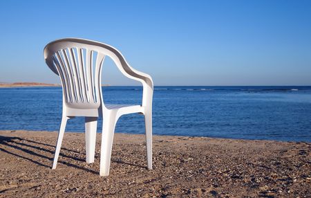 White chair at sand beach against blue seaの写真素材