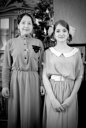 Vintage photo of daughter with mother against Christmas tree at homeの写真素材