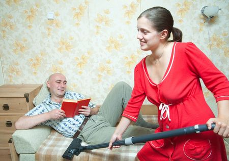 yang womam doing housecleaning and man resting over sofaの写真素材