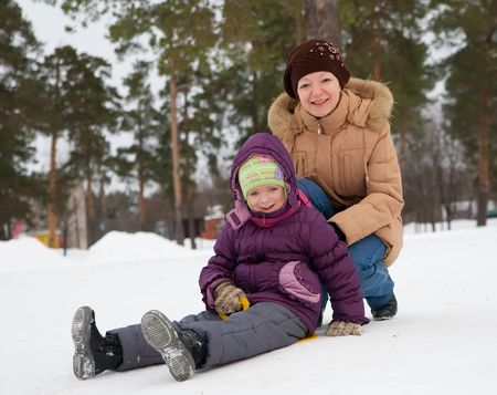 Little child sliding in the snow with  her motherの写真素材