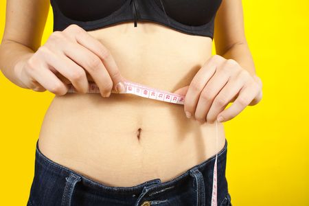 Girl measuring waist with tape measure over yellow backgroundの写真素材