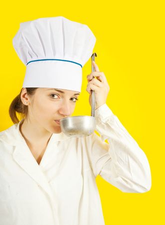 young woman in chef uniform tasting from ladle over yellow backgroundの写真素材