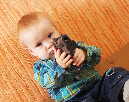 Little boy plays with gun in interiorの写真素材