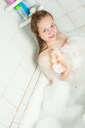 Long-haired girl washes with foam in bathの写真素材