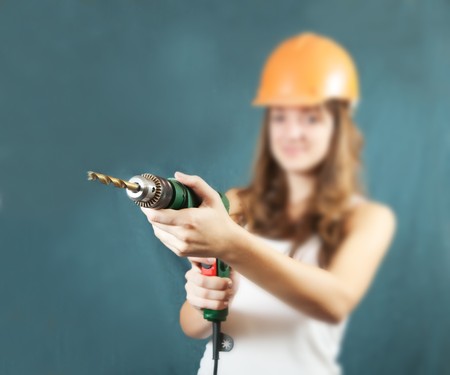 Female construction worker in a hard hat with drill over grey background. Focus on drill onlyの写真素材
