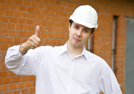 Happy builder with  thumbs up against  the brick wall