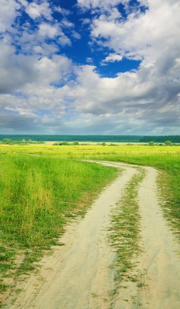 Country road through field under cloud in summerの写真素材