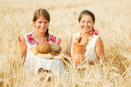 Women in traditional clothes with bread at cereals fieldの写真素材