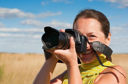 Senior woman photographer with camera  against summer fieldの写真素材