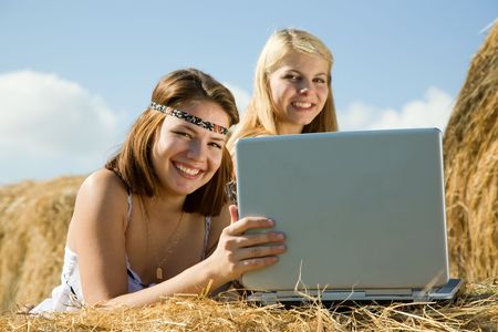 country girls with laptop on  hay at field. Focus on brunetteの写真素材