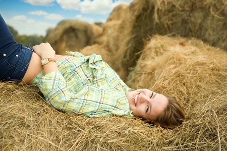 Pretty girl in checked shirt resting on straw baleの写真素材