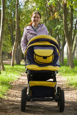 Happy mother walking with pram in parkの写真素材