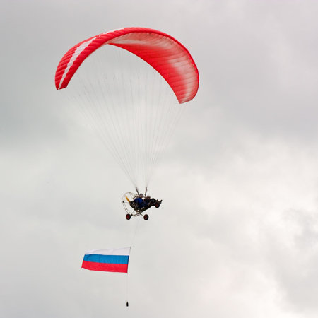 Paraglider with flag soaring against cloudy sky 