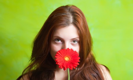 portrait of beauty brunette girl with red flower over green backgroundの写真素材