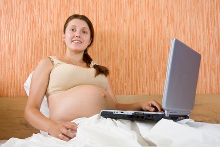 pregnant woman sitting on the sofa with laptopの写真素材