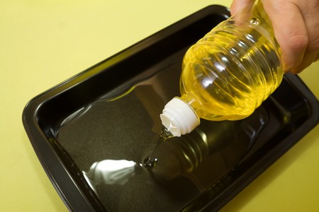 female hand adds  oil to roasting panの写真素材