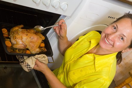 Mature woman cooking chicken on pan in ovenの写真素材