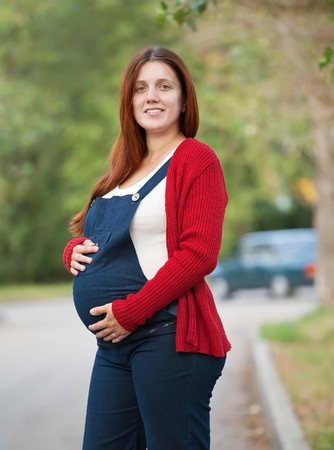 Portrait of  pregnant  woman holding belly in summer streetの写真素材