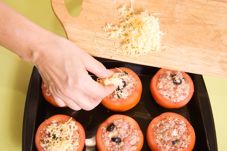 Closeup of cook adds cheese to stuffed tomato.See in series stages of cooking of stuffed tomatoの写真素材