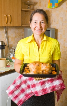 Mature woman with cooked stuffed chicken on roasting pan in kitchenの写真素材