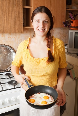 Young woman with  fried eggs and bacon in kitchen.
The end of preparation of bacon and eggs.  See seriesの写真素材