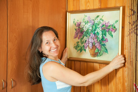 Mature woman hanging art picture on wall at home