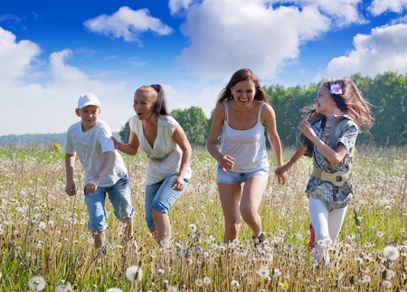 Four friends running at meadow in summerの写真素材