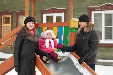 happy parents with  toddler playing on slide in winterの写真素材