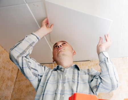 Man glues ceiling tile at homeの写真素材