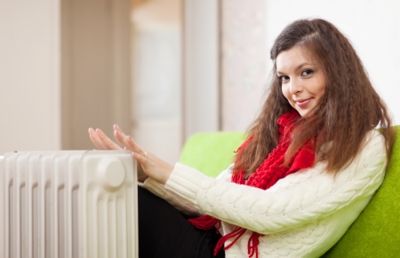 Pretty woman warms hands near calorifer at homeの写真素材
