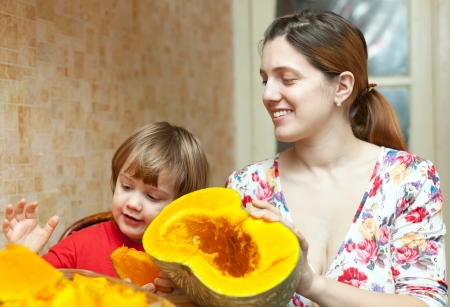 Happy mother with child cooks pumpkin  in  kitchen at her homeの写真素材