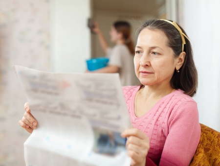mature woman reads newspaper during girl cleans at homeの写真素材