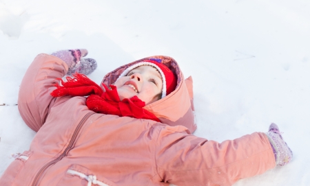 Happy baby girl lying down on the snow in winterの写真素材