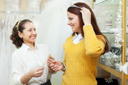 Mature saleswoman helps bride chooses bridal accessories at shop of wedding fashion. Focus on girlの写真素材