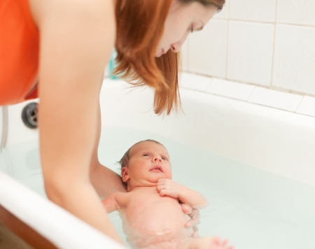 Mother bathes newborn baby in bath. Focus on childの写真素材