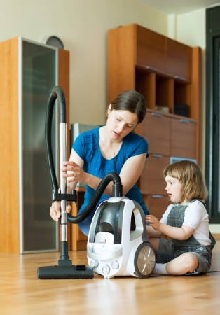 Woman teaches child to use the vacuum cleaner in living roomの写真素材