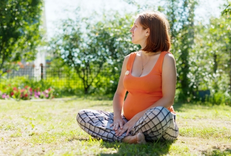 pregnant woman sits on grass in  summer parkの写真素材